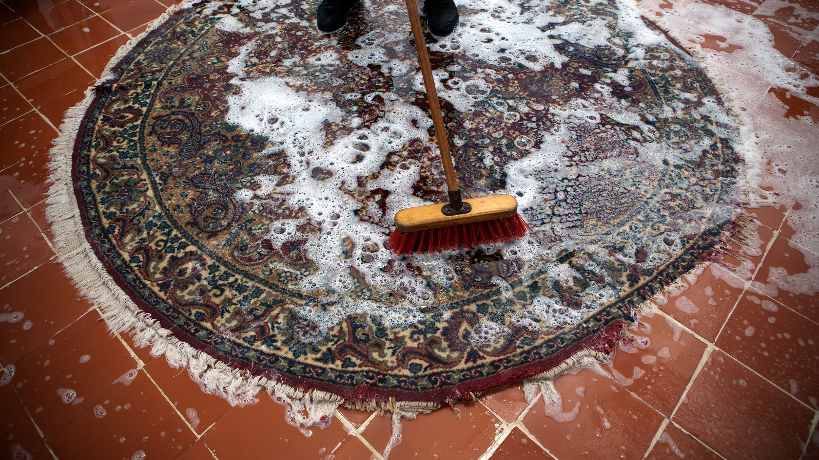 A person cleaning a rug with a broom